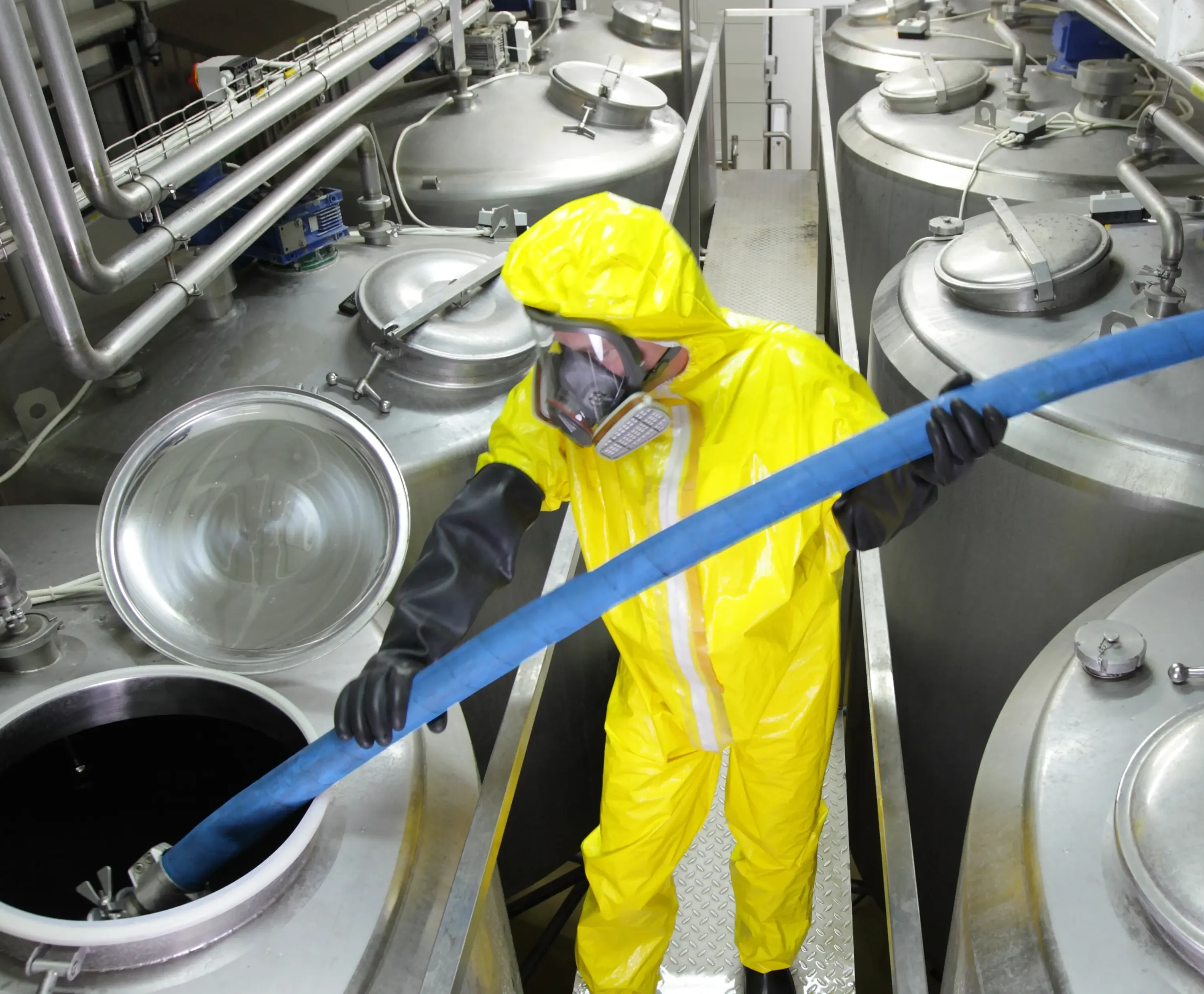 Chemical operative in coveralls fills massive silver tank at fine chemicals facility.