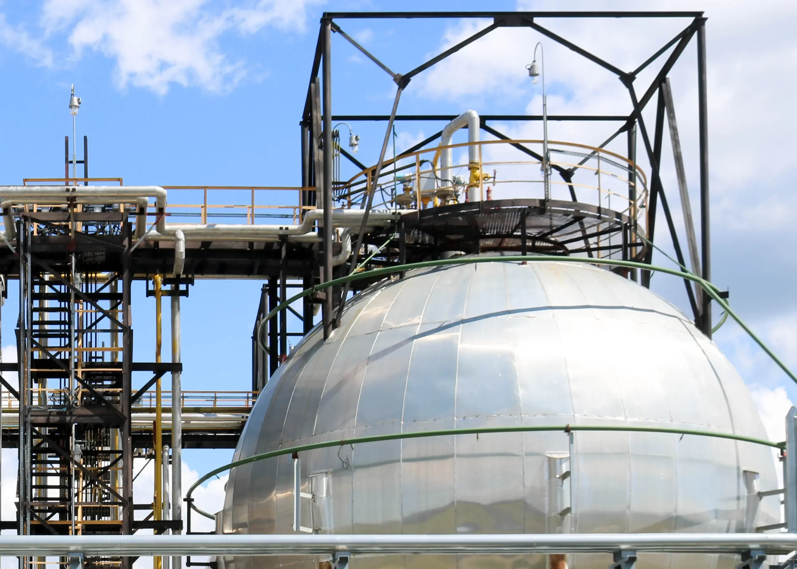 A robust, shiny metal ammonia storage tank with pipes and equipment is used in the petrochemical refinery for high-pressure iron storage.