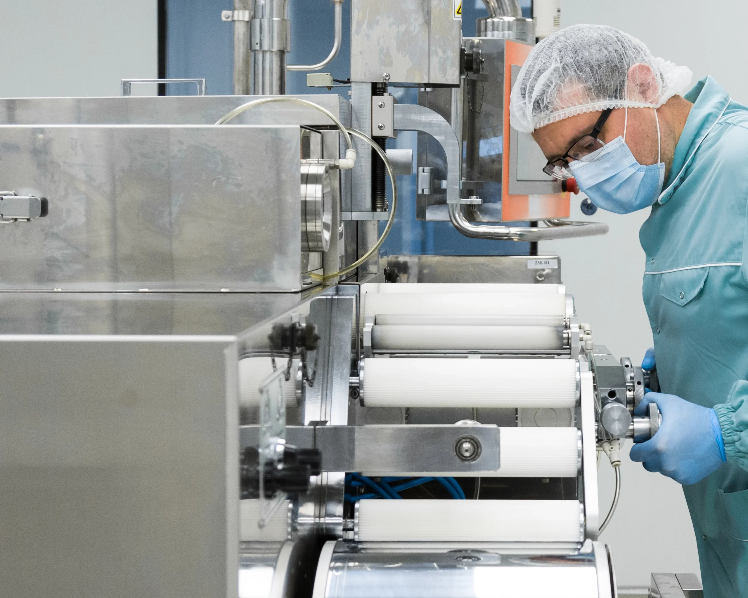 In a highly sanitized environment, a diligent worker in protective attire can be seen operating pharmaceutical equipment within a pharmacy industry factory