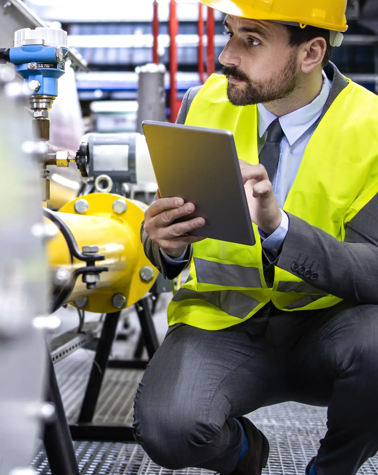 A focused man in protective gear inspects refinery pipes with a tablet, analyzing data and ensuring smooth operations.